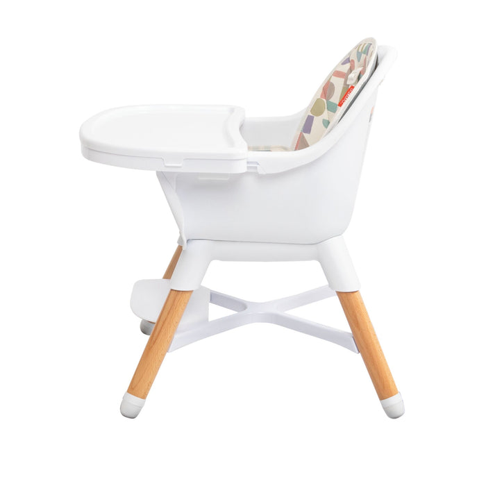 The Nuby 4-in-1 Multi-Use High Chair | White Geometrics features a white plastic seat and tray, wooden legs with white tips, a geometric cushion, and a white footrest. This adjustable high chair grows with your child.