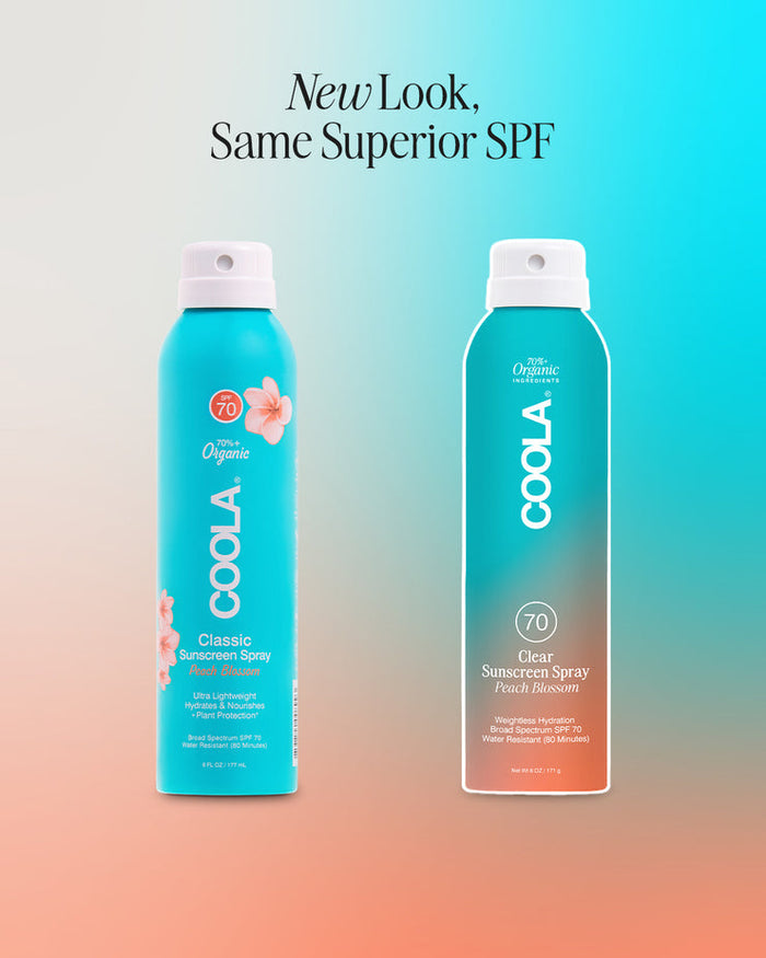 Two blue spray bottles of Classic Body Organic Sunscreen Spray SPF 70 | COOLA with peach blossom scent, showcasing the new and old packaging designs side by side.