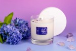 I Choose Pride Candle | Aluminate Life in a clear glass jar, surrounded by purple flowers and small crystals on a soft lavender surface, creating a calming wellness ambiance.