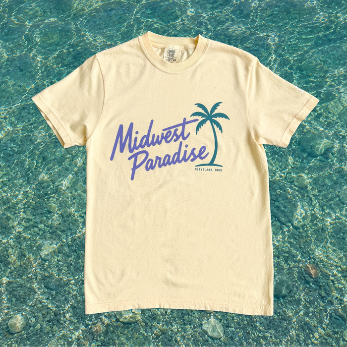 Beige t-shirt with 'Midwest Paradise' text and palm tree graphic on a blue water background