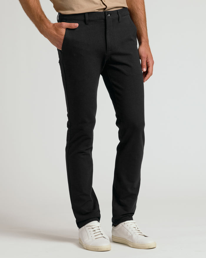 Black Slim Chino Pants 2.0 with white sneakers, hand in pocket.