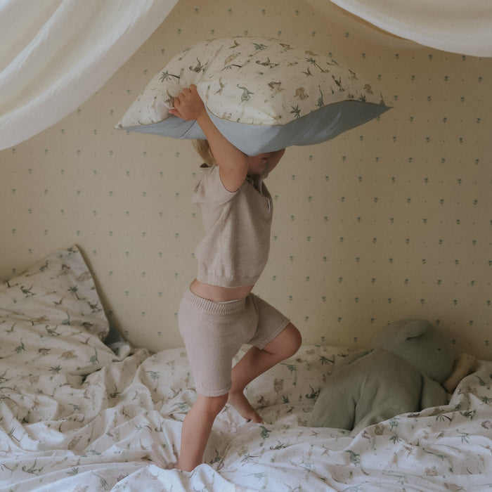 Dino Dreams Standard Pillowcase in Sage with child jumping on bed holding pillow in the air