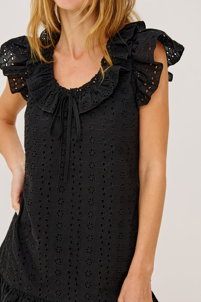 Essie Mini Dress in Cotton Voile With Eyelet Detailing, A-Line Silhouette, Wide Scoop Neckline With Ruffle Trim, Flutter Sleeves, and is Fully Lined in Black Eyelet Colorway - Upper Body Front View Featured on Model