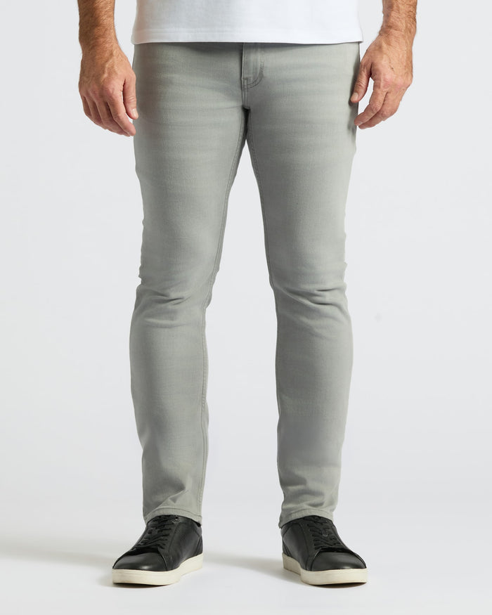 Front view of a man wearing Gray Medium Indigo Slim Comfort Stretch Jeans 3-Pack paired with black sneakers against a plain white background.