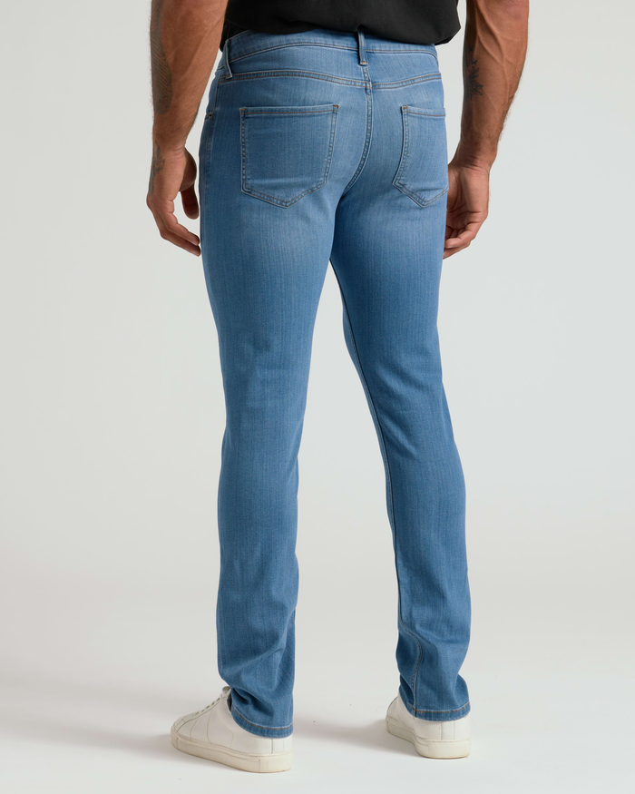 Man wearing Medium Indigo Wash Slim Comfort Stretch Jeans shown from the back, paired with white sneakers and a black shirt, highlighting the slim fit and stretch fabric.