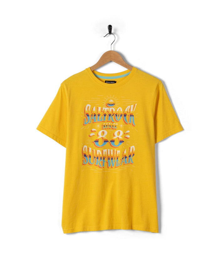 The Saltrock Mex Logo Men's T-Shirt in yellow features a colorful surfwear graphic with sun, waves, and sunglasses, classic crew neckline, and bold Saltrock branding. Displayed on a hanger against a white background.