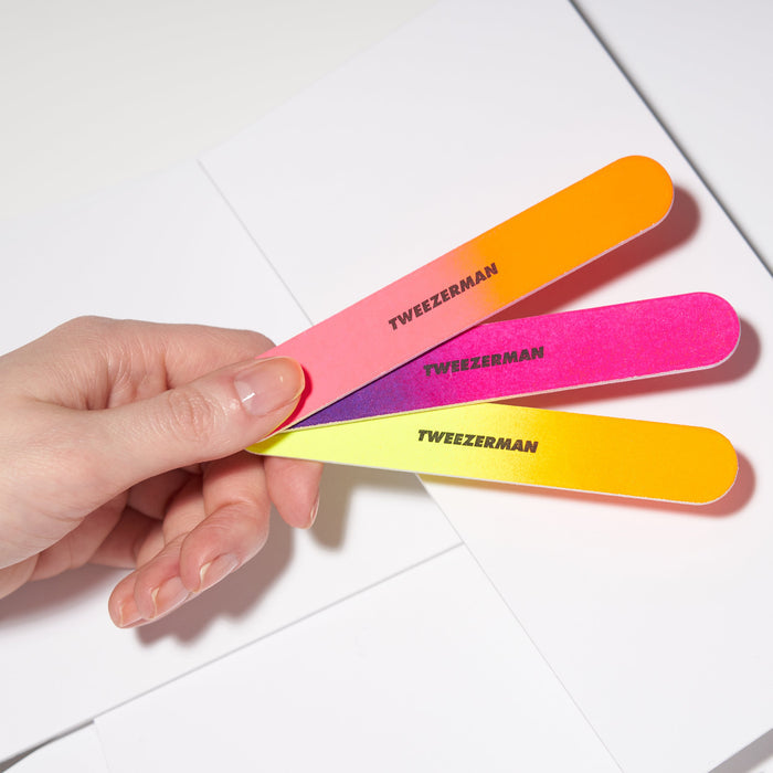 Hand holding three neon colored nail files in orange, pink, and yellow labeled with "Tweezerman" from the Neon Filemate Set | Tweezerman.