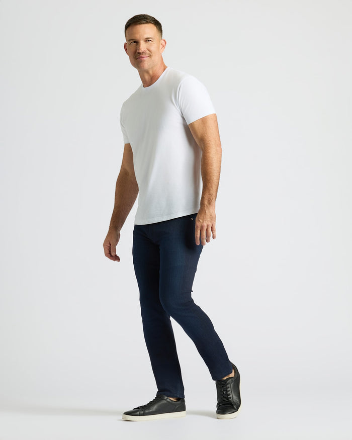 Man wearing a white t-shirt and dark blue leggings on a light gray background