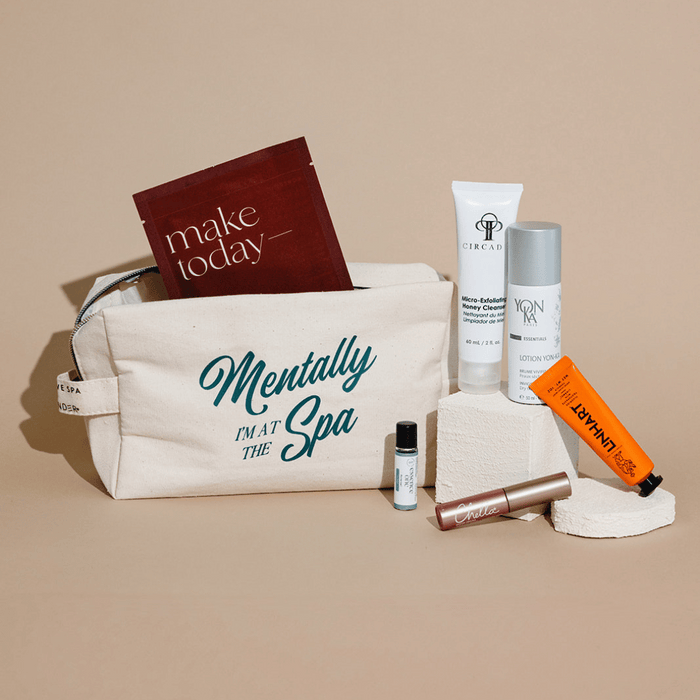 Canvas travel pouch with "Mentally I'm at the Spa" text, containing skincare and wellness products arranged around it, featured in the Spafinder Travel Kit | Live Love Spa.