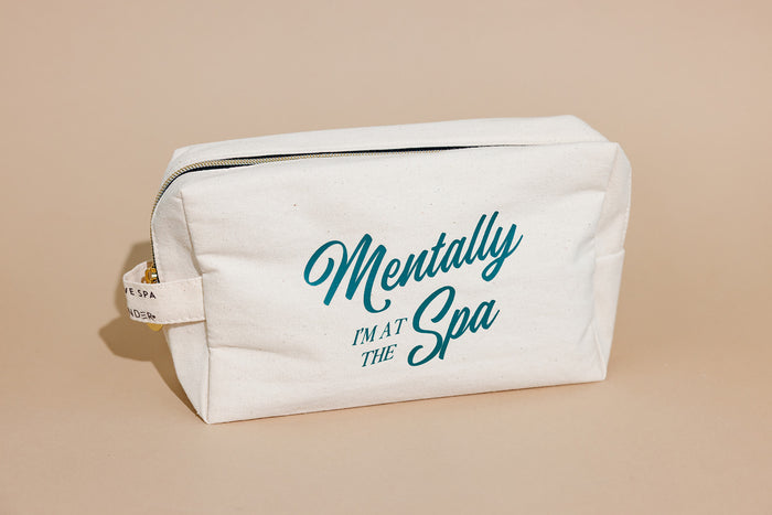 A cream-colored canvas travel pouch with a zipper and the phrase "Mentally I'm at the Spa" printed in teal, part of the Spafinder Travel Kit | Live Love Spa collection.