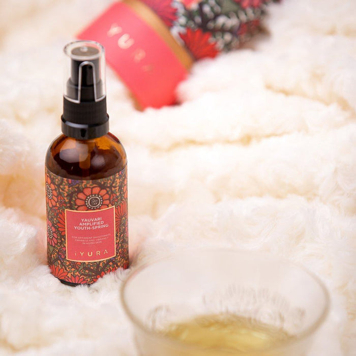 Amber spray bottle with floral label placed on a soft white fabric background next to a blurred tea cup, styled for Spafinder Travel Kit | Live Love Spa.