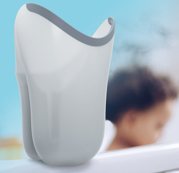 The Tear-Free Rinse Pail, a white flexible baby bath pail with an easy-grip handle and gray edge, is shown in the foreground, while a young child stands near a bathtub in the blurred background.